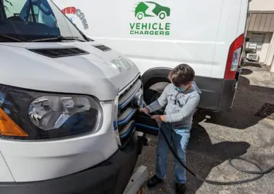 A man is charging a vehicle in front of a white van.