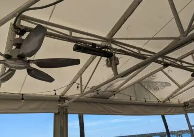 A ceiling fan hanging from a tent on the beach.